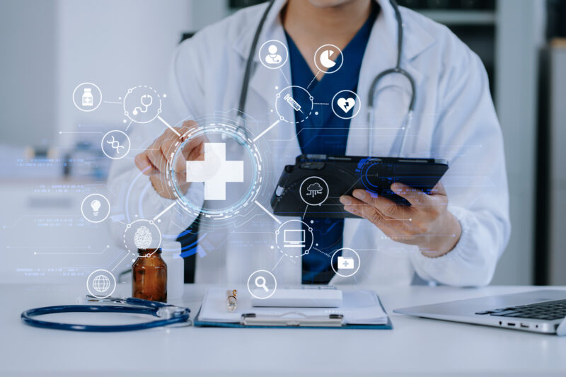 Doctor Working On Laptop And Tablet And Medical On Clipboard On Desk, Electronics Medical Record System Emrs Concept. Doctor Working On Laptop And Tablet And Medical On Clipboard On Desk, Electronics Medical Record System Emrs Concept.